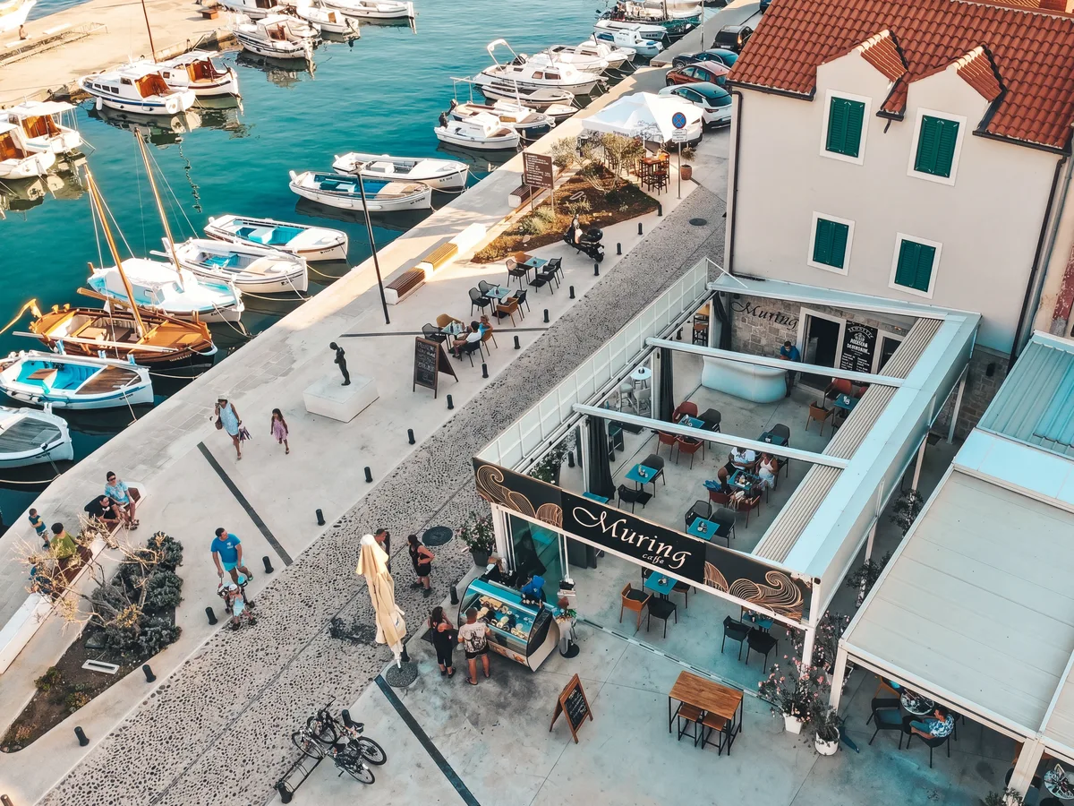 Caffe Bar Muring Murter – pogled dronom na terasu kafića uz marinu, brodovi u pozadini