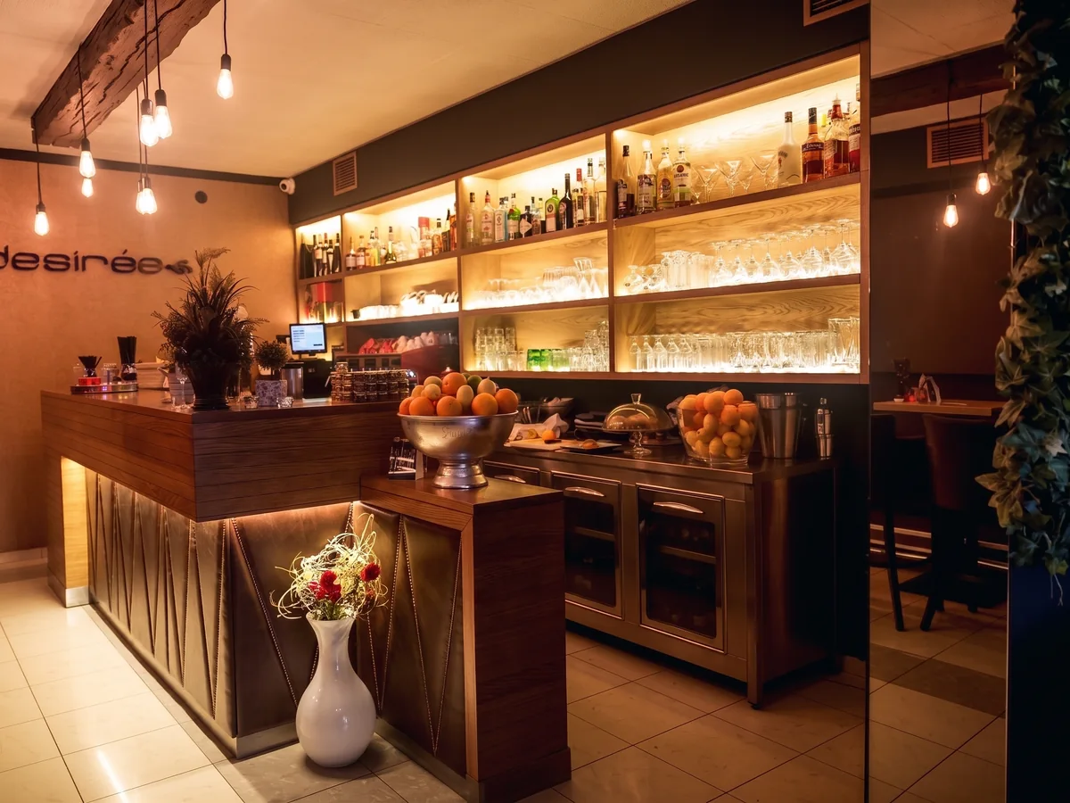 Desirée – bar šank s osvijetljenim regalima boća, voćem za koktele i 