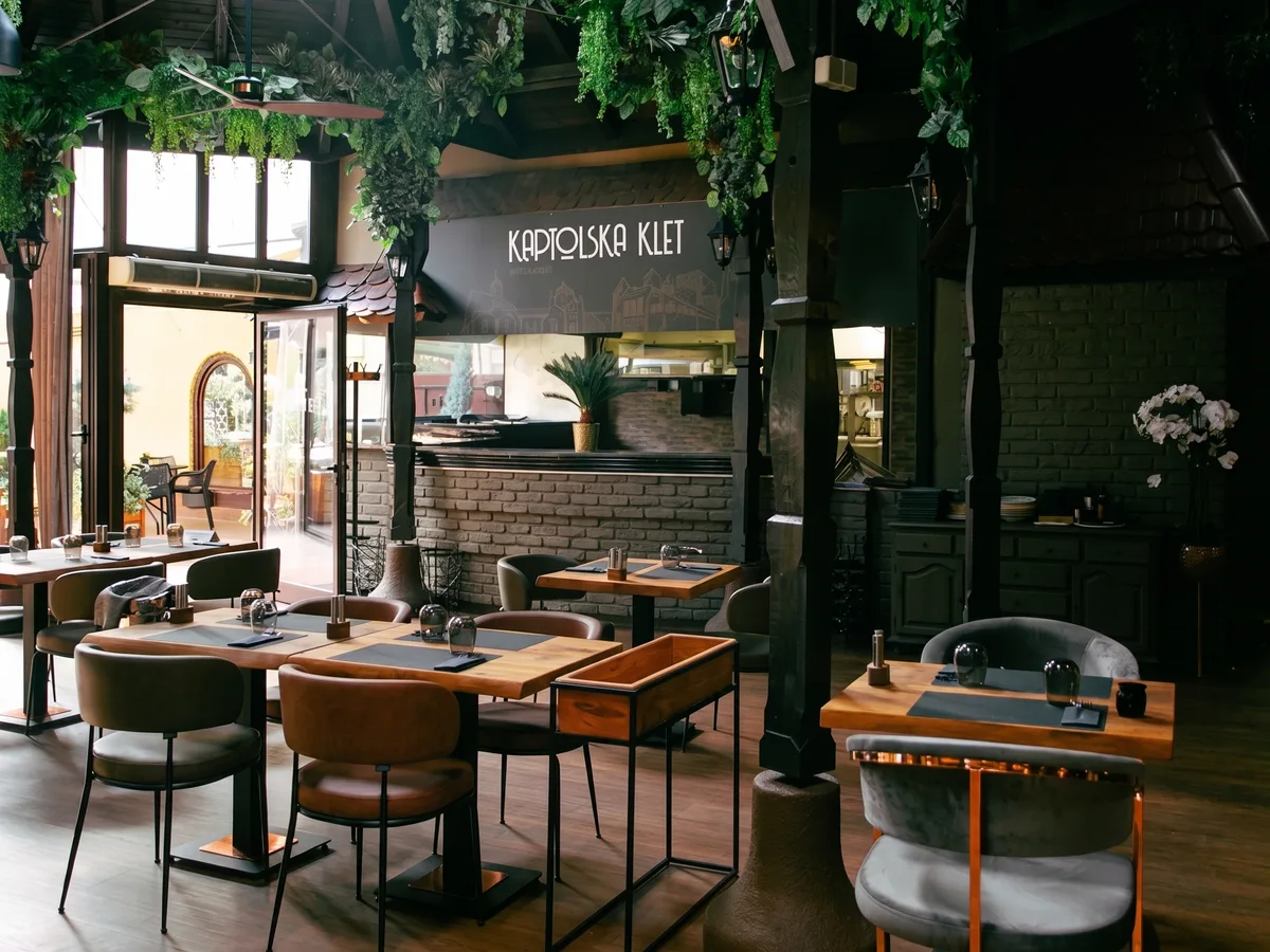 Kaptolska Klet – main dining room with branded wall, wooden tables and open kitchen