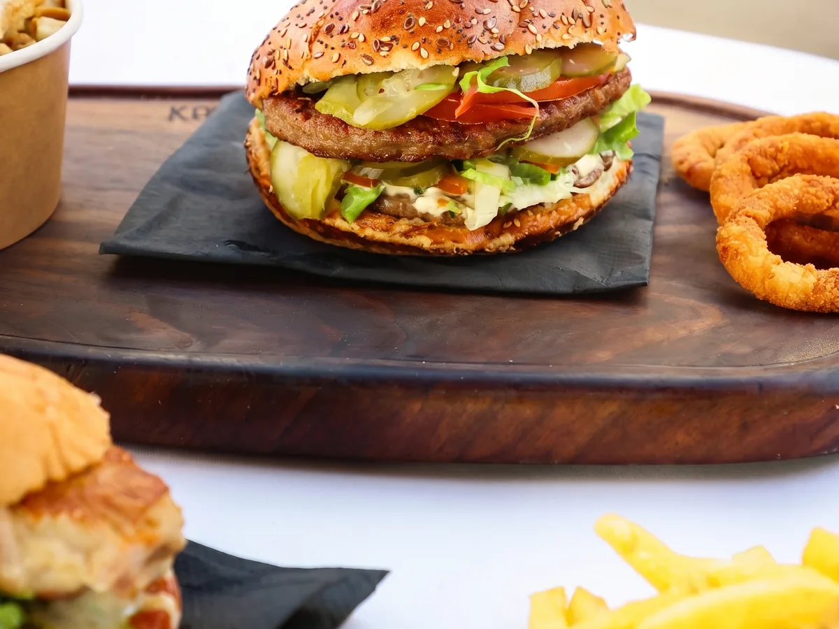 Pingvin – tall beef burger on a wooden board with onion rings and fries, Zagreb